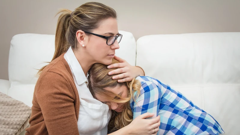 Två kvinnor sitter i en soffa och kramar om varandra.
