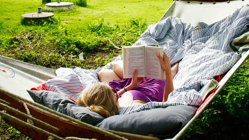 En kvinna som ligger i en hängmatta och läser en bok.