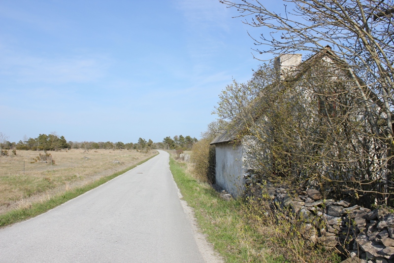 Ett vitt hus med en stenmur, en skorsten på taket och huset ligger precis vid landsvägen.
