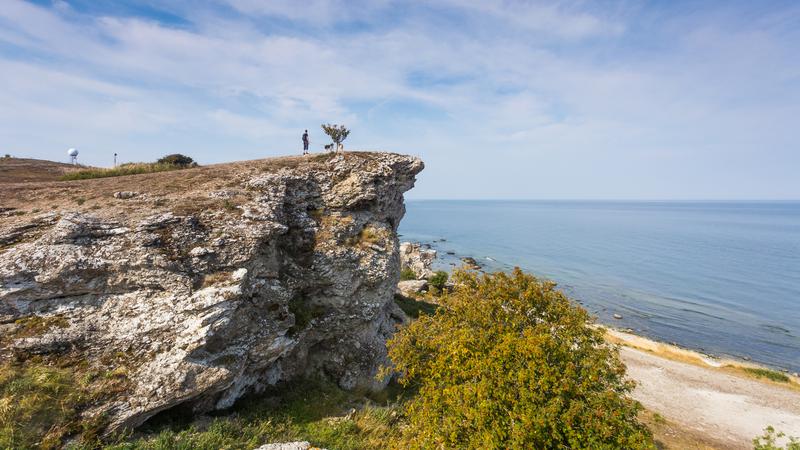 En person står på en klipp vid Hoburgskusten på Gotland och ser ut över havet.