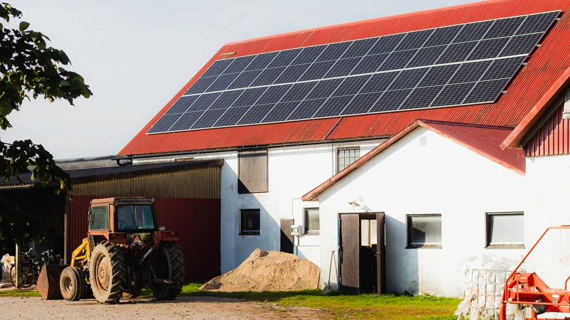 En traktor parkerad framför ett hus med en solpanel på taket.