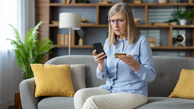 En kvinna som sitter på en soffa och tittar på sin mobiltelefon.