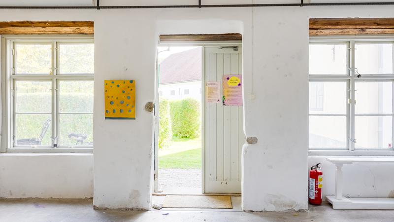 En vitkalkad vägg med stora fönster och en öppen dörr
