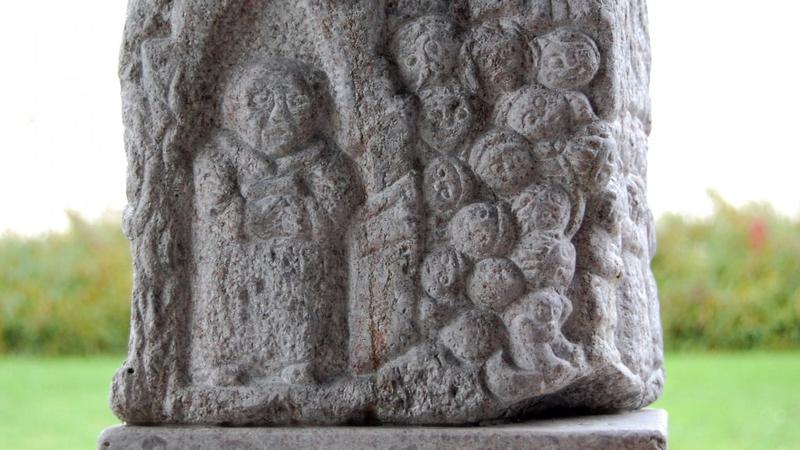En stenskulptur visar en stor figur och många mindre ansikten