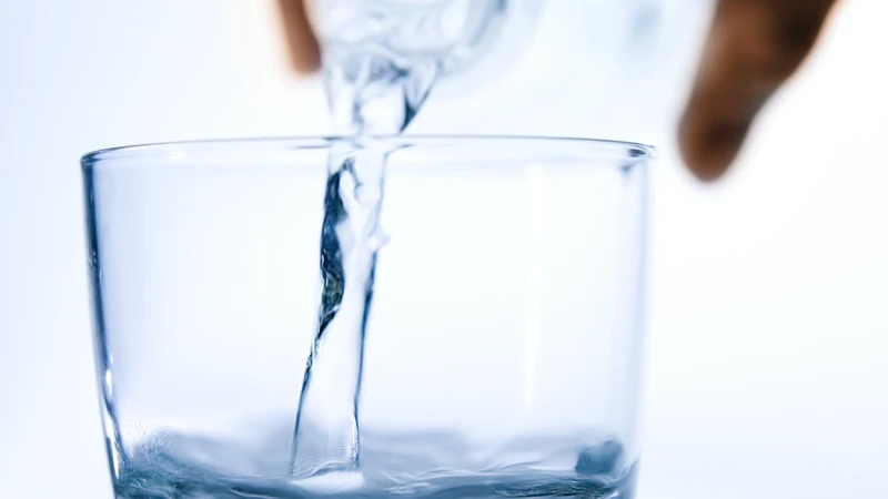 En hand häller vatten i ett glas.