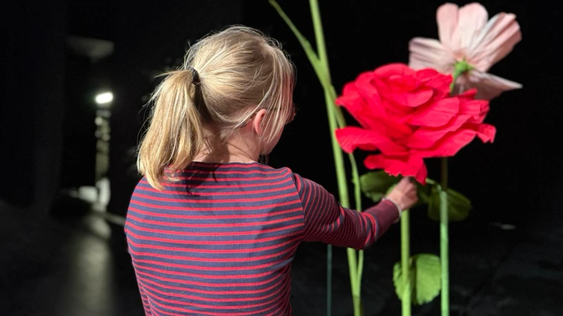 En flicka står bredvid en vas med blommor.