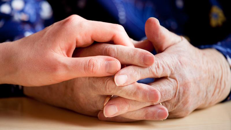 Bild på vårdpersonals händer som håller patients hand.