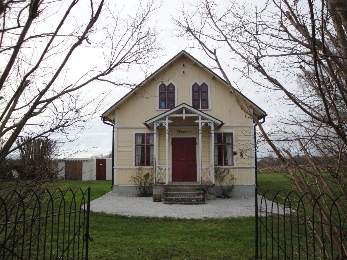 Ett gult hus med träfasad, rödvita fönster och en röd ytterdörr.