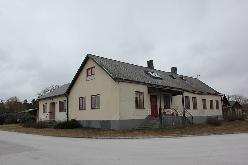 Ett beige hus med röda dörrar, röda fönster och ett svart tak.