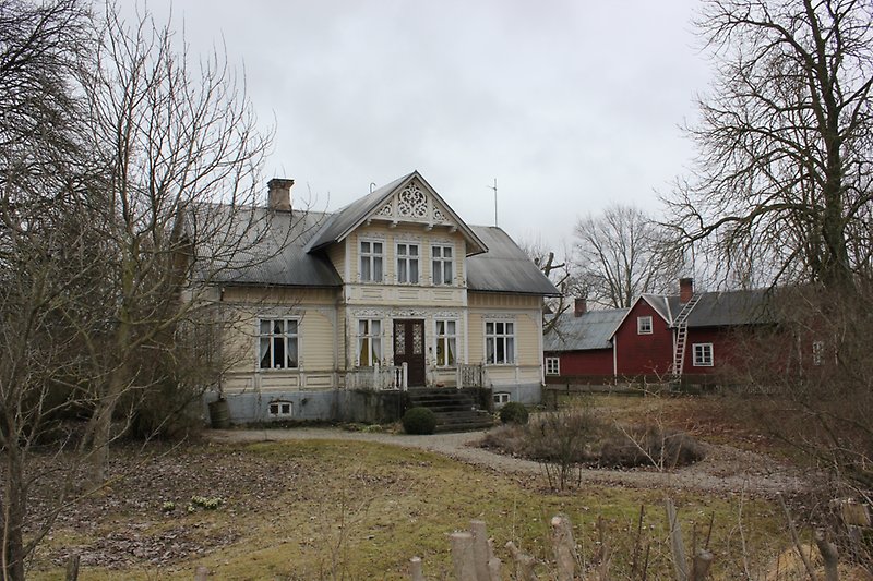 Ett ljusgult hus med vita fönster, en svart ytterdörr och ett grått plåttak.