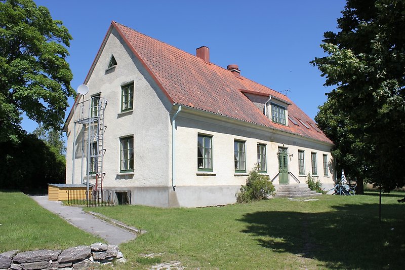 En vit byggnad med gröna fönster, en grön ytterdörr och ett rött tak med två skorstenar.