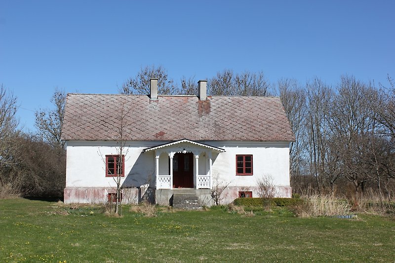 Ett vitt hus med röda fönster, en röd ytterdörr, ett rött tak med en skorsten.