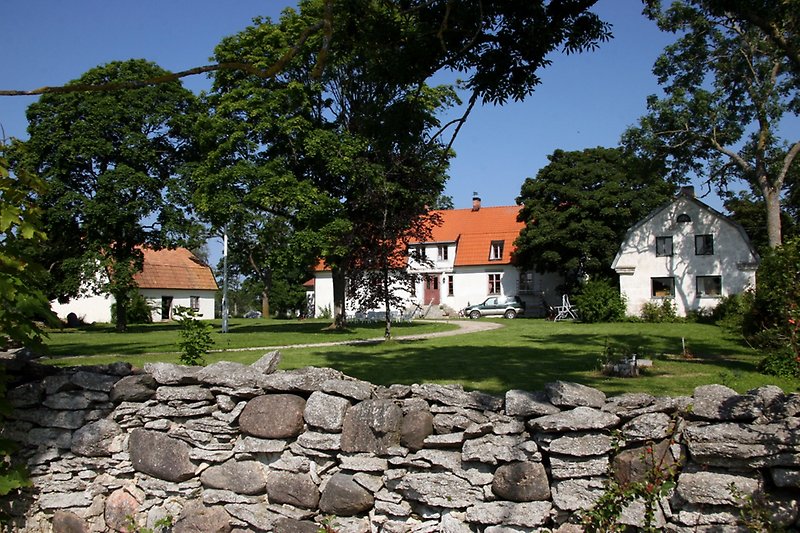 Ett staket av natursten, nyklippt gräsmatta och flera vita byggnader.