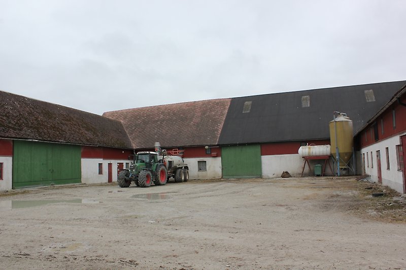 En rödvit lada med gröna portar, röda dörrar och röda fönster. Utanför ladan står det en grön traktor.