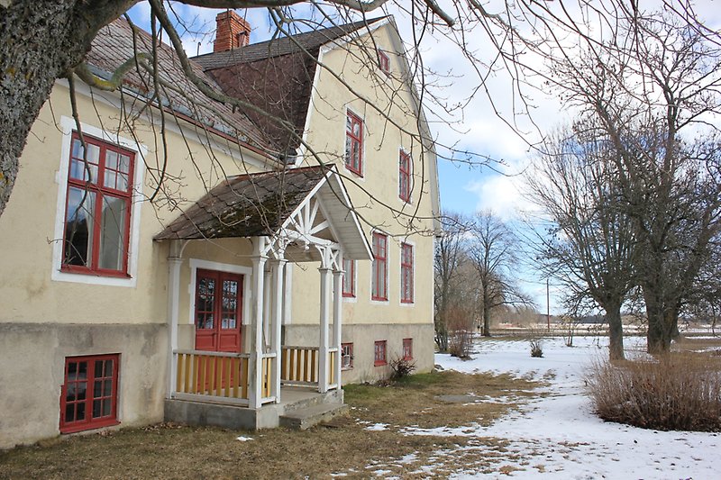 Ett ljusgult hus med röda fönster och en röd ytterdörr.