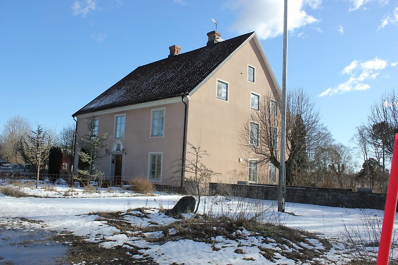 Ett beige hus med ljusgröna fönster och två skorstenar.