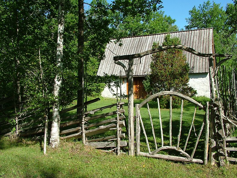 Ett vitt hus, ett trästaket och en trägrind nära ett skogsområdet.