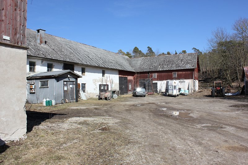 Gårdsmiljön präglas av en rödvit ladugård, en traktor och en bil.