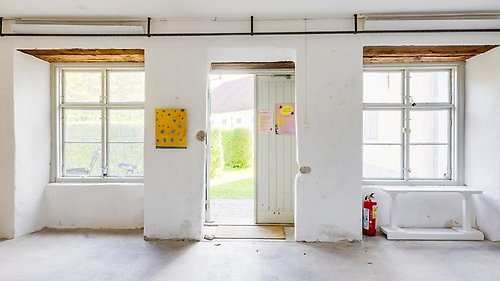 En vitkalkad vägg med stora fönster och en öppen dörr