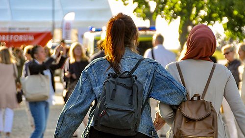 Två personer går ifrån kameran mot andra personer som står längre bort