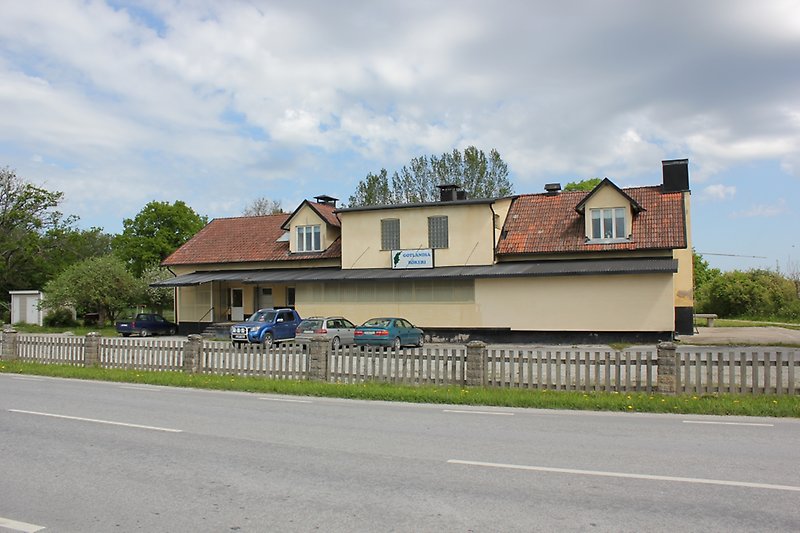 Längs vägen ligger det en ljusgul byggnad med ett rött tegeltak.