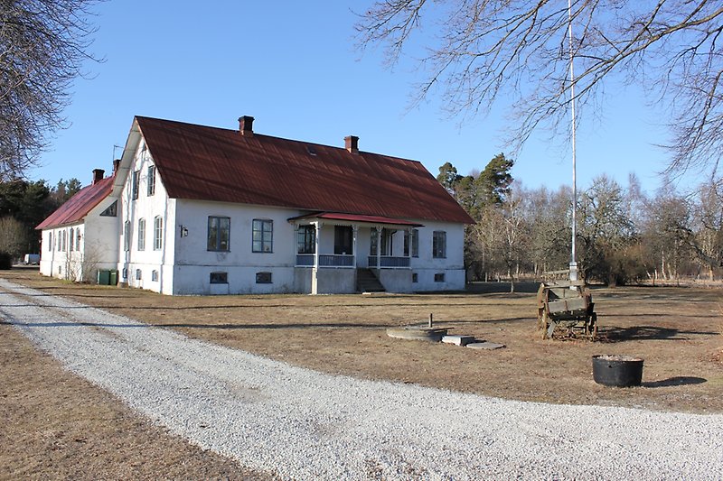 Ett vitt tvåvåningshus med blåa fönster och ett rött tak med två skorstenar.