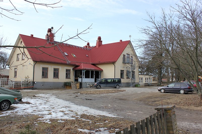En ljusgul skolbyggnad med bruna fönster och ett rött plåttak.
