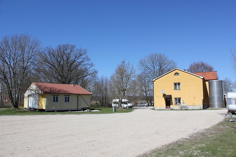En gul tvåvåningsbyggnad med vita fönster och ett rött tak samt en liten gul trästuga.