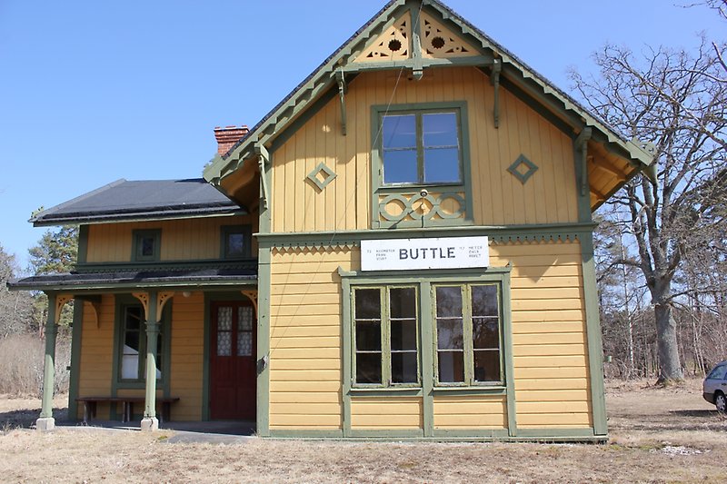 En gulgrön träbyggnad med gröna fönster och en röd ytterdörr.