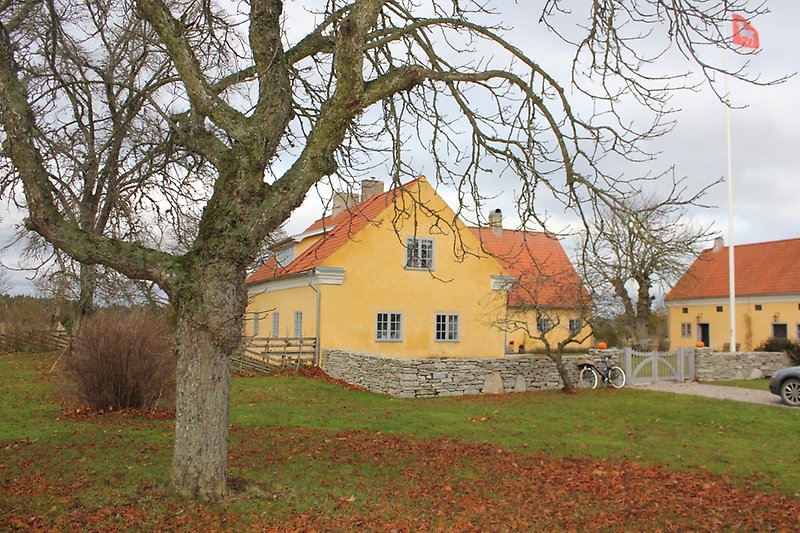 Tre gula byggnader med gråa fönster, svarta dörrar och röda tegeltak.
