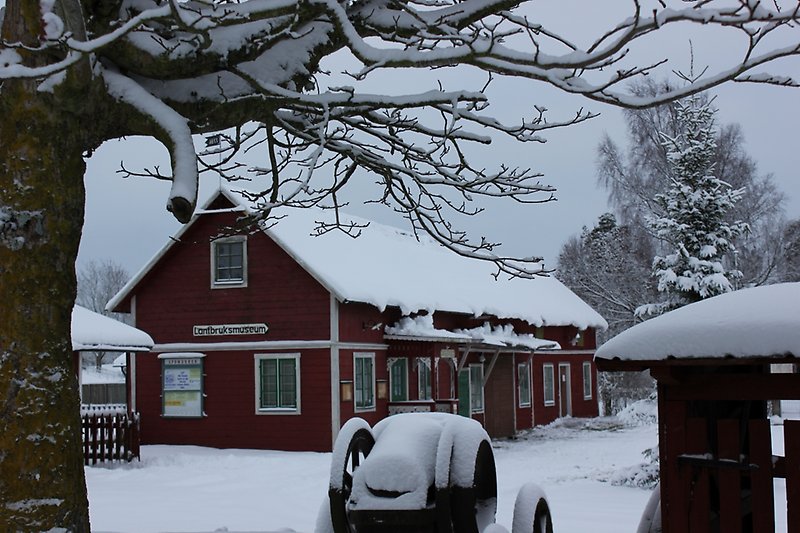 En röd träbyggnad med gröna fönster och ett tak täckt av snö.