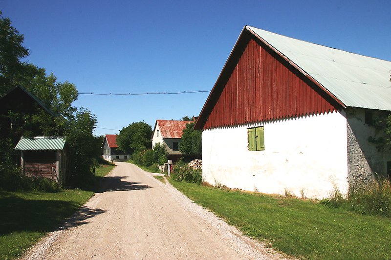 På höger sida av grusvägen ligger det en rödvit lada.