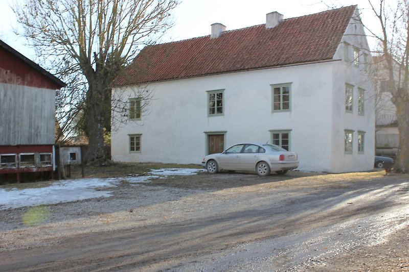 Ett vitt tvåvåningshus med gröna fönster och ett rött sadeltak.