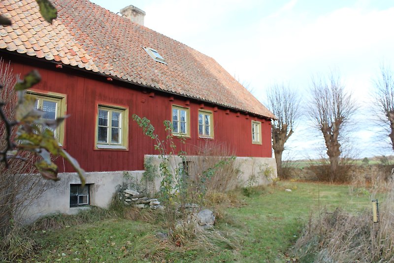 Ett rött envåningshus med träfasad, gröna fönster och ett rött tegeltak med en skorsten.
