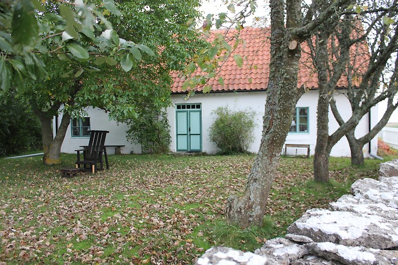Ett vitt litet hus med små gröna fönster, grön ytterdörr och ett rött tak.