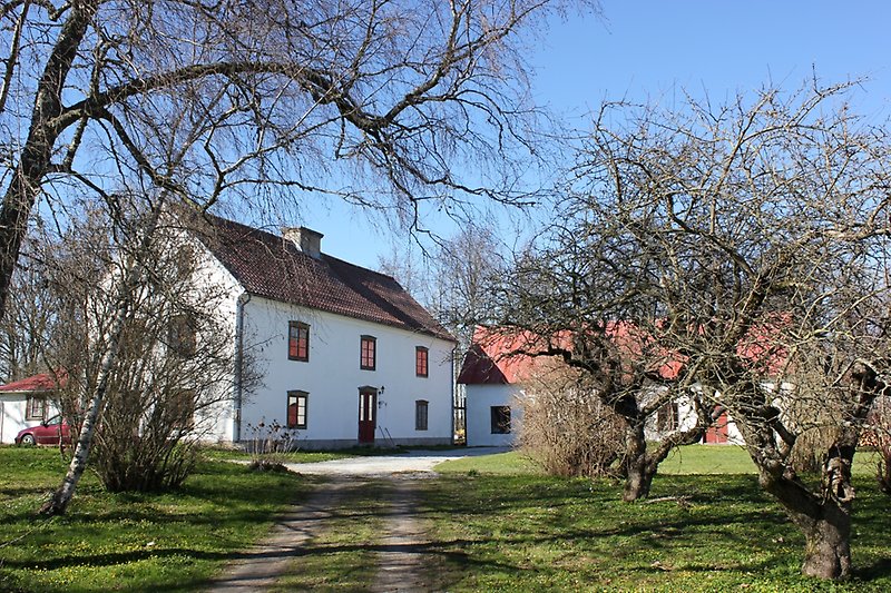 Ett vitt hus bestående av två våningar med röda dörrar, röda fönster och ett brunt tegeltak.