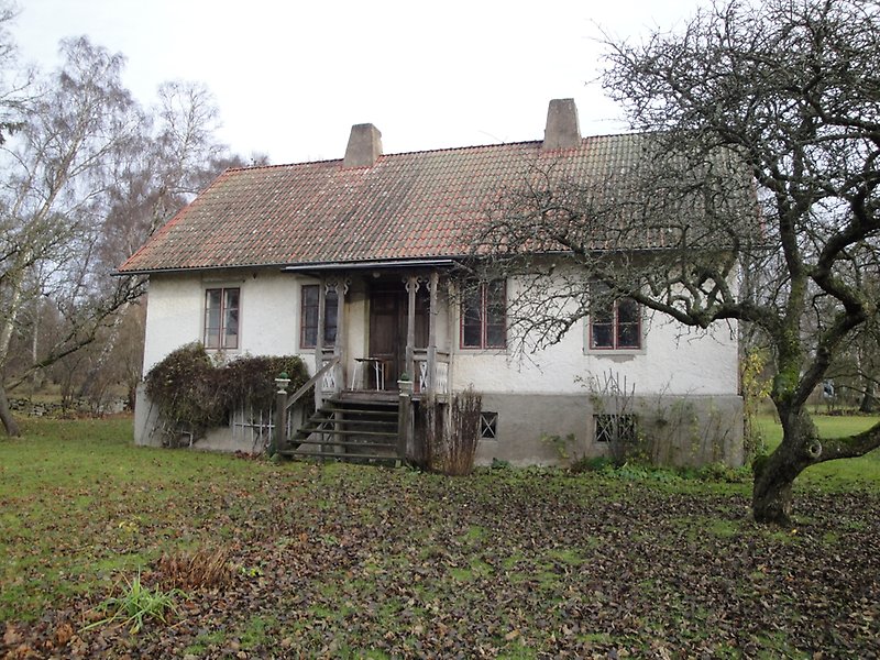 Envånings vitt hus med två skorstenar, ett rött tak och röda fönster.