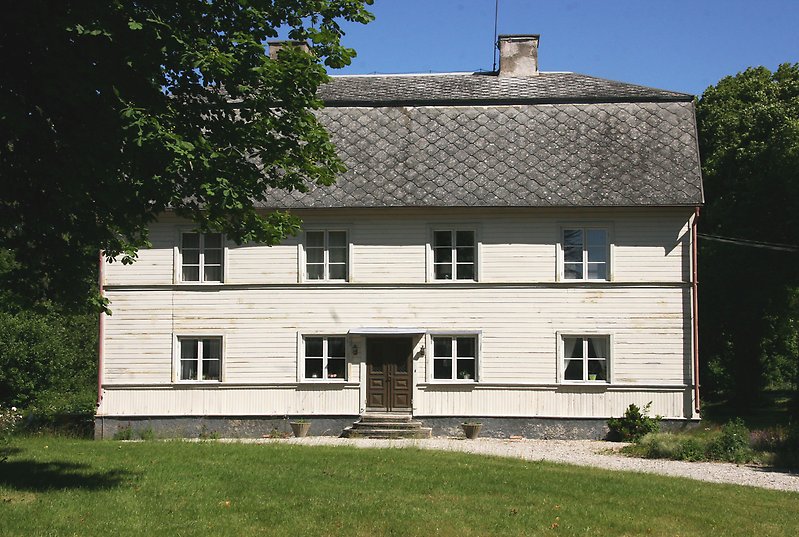 Ett tvåvåningshus med vit träfasad, vita fönster och ett svart tak.