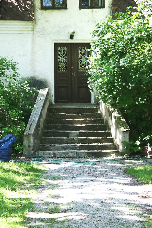 Gaveln på ett vitt stenhus med ett svart tak, svarta fönster och en gammal trappa nedanför en svart ytterdörr.