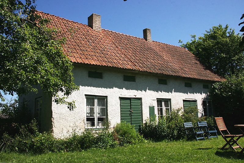 Ett vitt envåningshus med gröna dörrar, vita fönster och ett rött tak med två skorstenar.