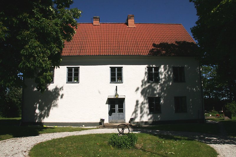 Ett vitt tvåvåningshus med blåa fönster, ett rött tak med två skorstenar och en blå ytterdörr.