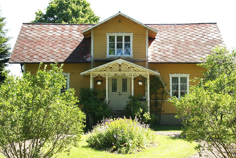 Ett gult hus med träfasad, vita fönster och ett rött tak.