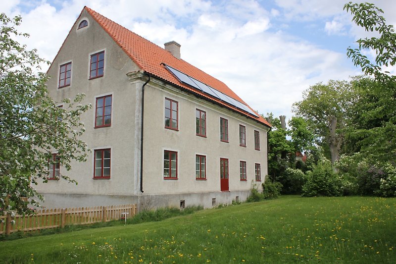 Tvåvåningshus med rött tak, solpaneler och röda fönster.