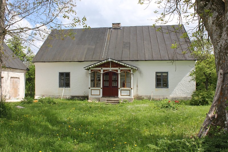 Ett vitt hus med en röd ytterdörr, blåa fönster och ett svart tak.