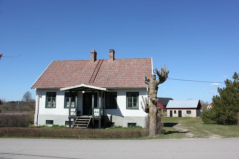 Ett vitt hus med gröna fönster, grön ytterdörr och ett rött tak.