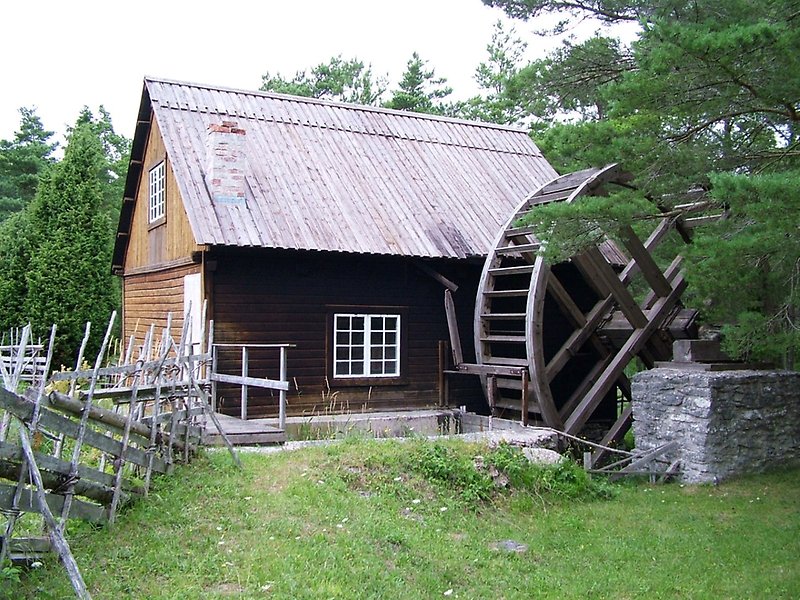 Gammal vattenkvarn med trästaket, skorsten och plåttak.