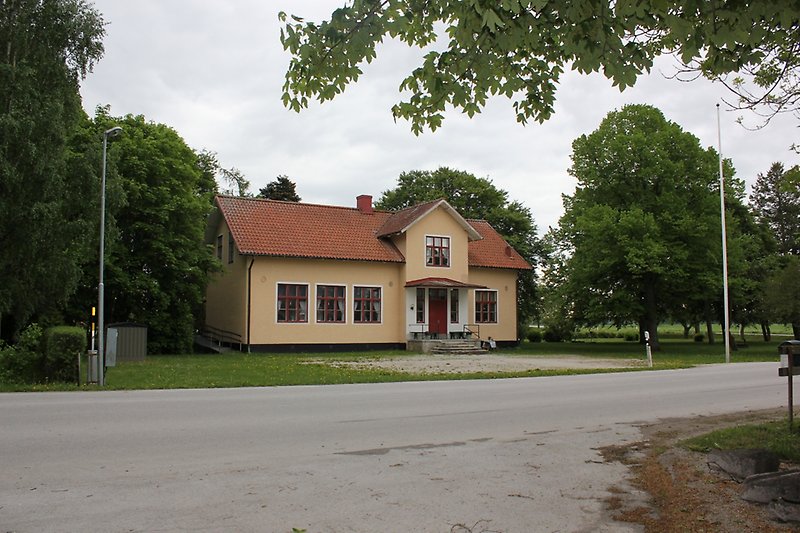 Ett gult hus som ligger längs vägen har röda fönster, röd ytterdörr och ett orange tak.