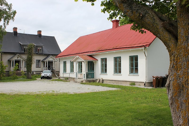 Två vita byggnader med gröna fönster, den ena har ett svart plåttak och den andra har ett rött plåttak.