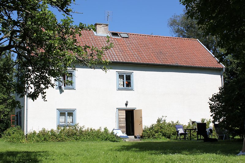 Ett vitt hus med små ljusblåa fönster, ett rött tak och en skorsten.
