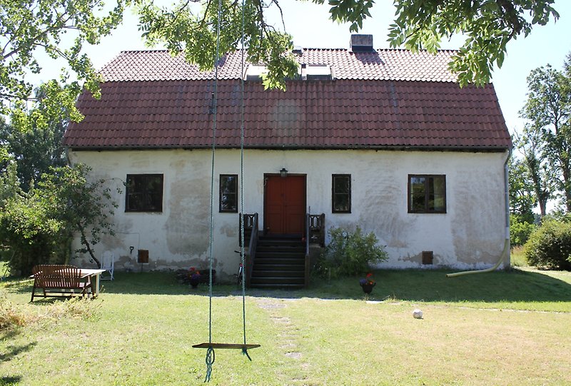 Ett vitt hus med putsade väggar, svarta fönster, en brun ytterdörr och ett rött tak.